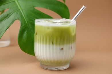 Photo of Glass of tasty iced matcha latte and leaf on light brown background, closeup