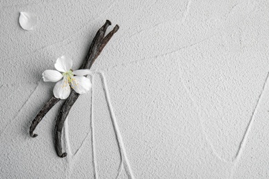 Photo of Flat lay composition with aromatic vanilla sticks and flower on light background, space for text