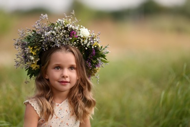 Photo of Cute little girl wearing wreath made of beautiful flowers in field