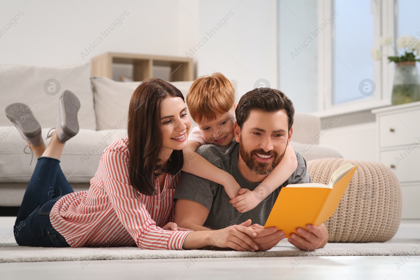 Photo of Happy parents with their child reading book on floor at home