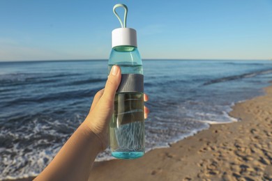Woman holding glass bottle with water near sea, closeup