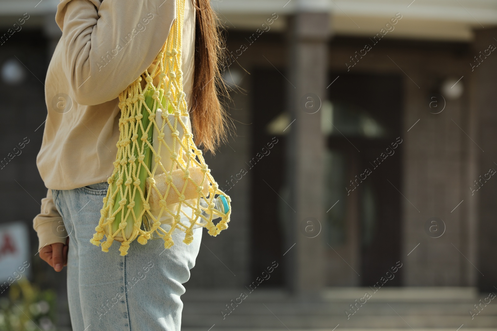 Photo of Conscious consumption. Woman with net bag of eco friendly products outdoors, closeup. Space for text