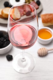 Glass of delicious rose wine and snacks on white table, closeup