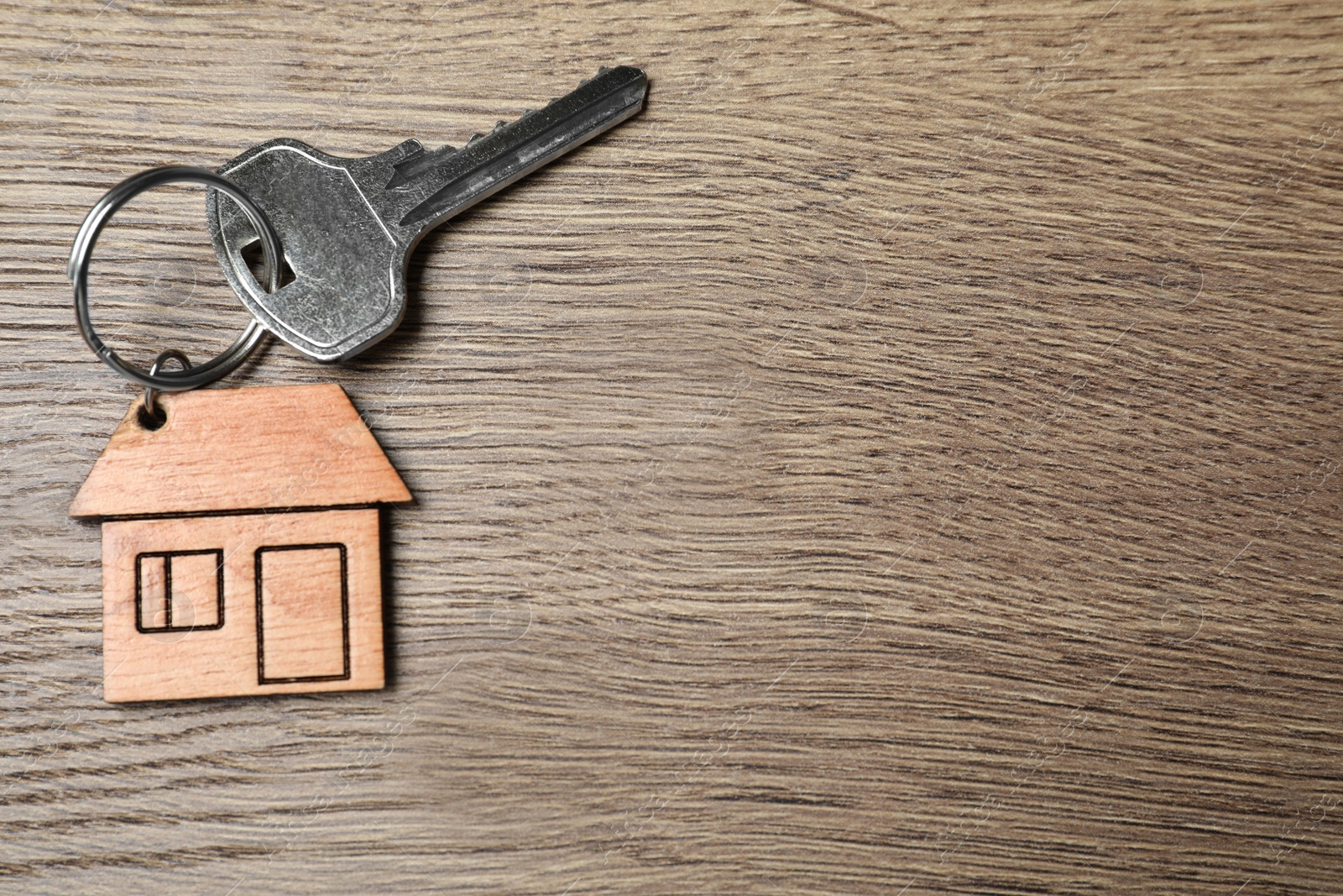 Photo of Key with trinket in shape of house on wooden background, top view and space for text. Real estate agent services