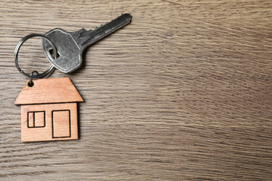 Photo of Key with trinket in shape of house on wooden background, top view and space for text. Real estate agent services