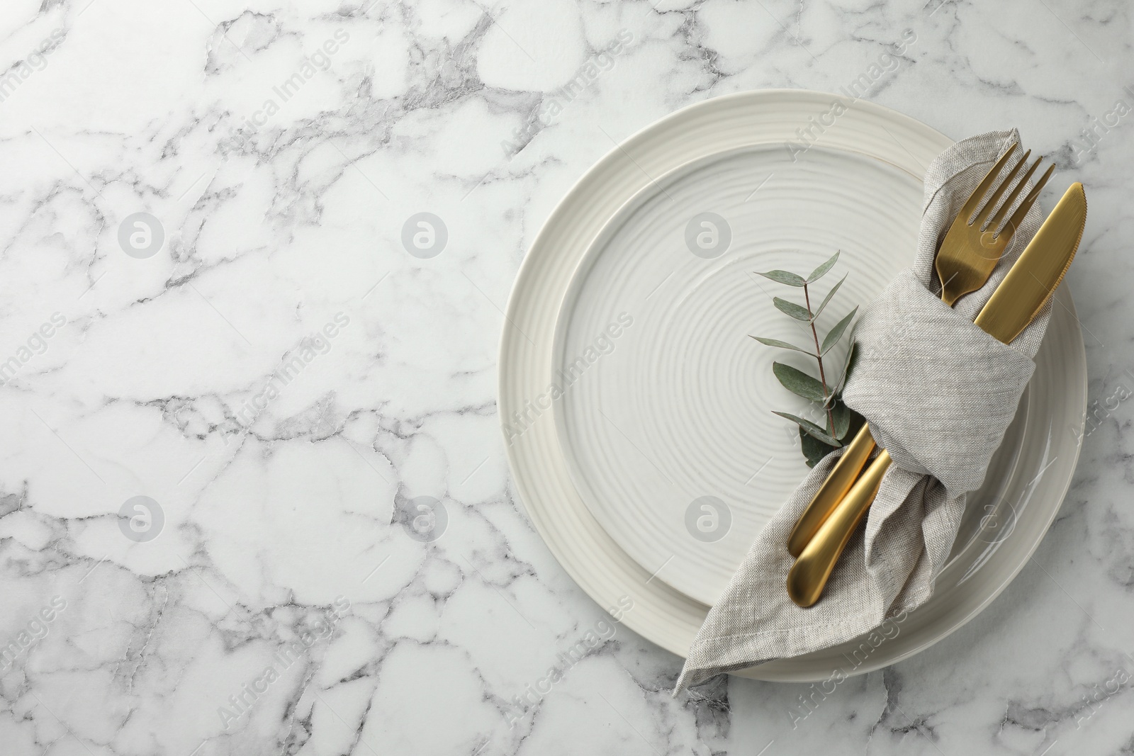 Photo of Stylish setting with cutlery, napkin, eucalyptus branch and plates on white marble table, top view. Space for text