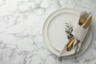 Stylish setting with cutlery, napkin, eucalyptus branch and plates on white marble table, top view. Space for text