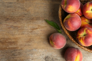 Photo of Wicker bowl with tasty peaches on rustic wooden table, top view. Space for text