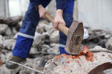 Man breaking brick with sledgehammer outdoors, selective focus