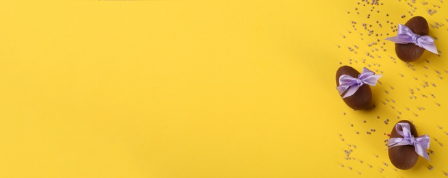 Image of Sweet chocolate eggs on yellow background, flat lay with space for text. Banner design