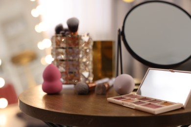 Photo of Different beauty products and mirror on wooden table in makeup room, closeup