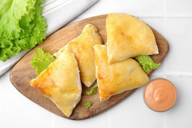 Delicious samosas with lettuce and sauce on white tiled table, flat lay