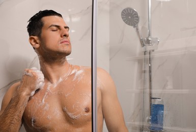 Photo of Handsome man with sponge taking shower at home