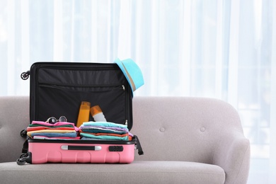 Modern suitcase full of clothes on sofa indoors. Space for text