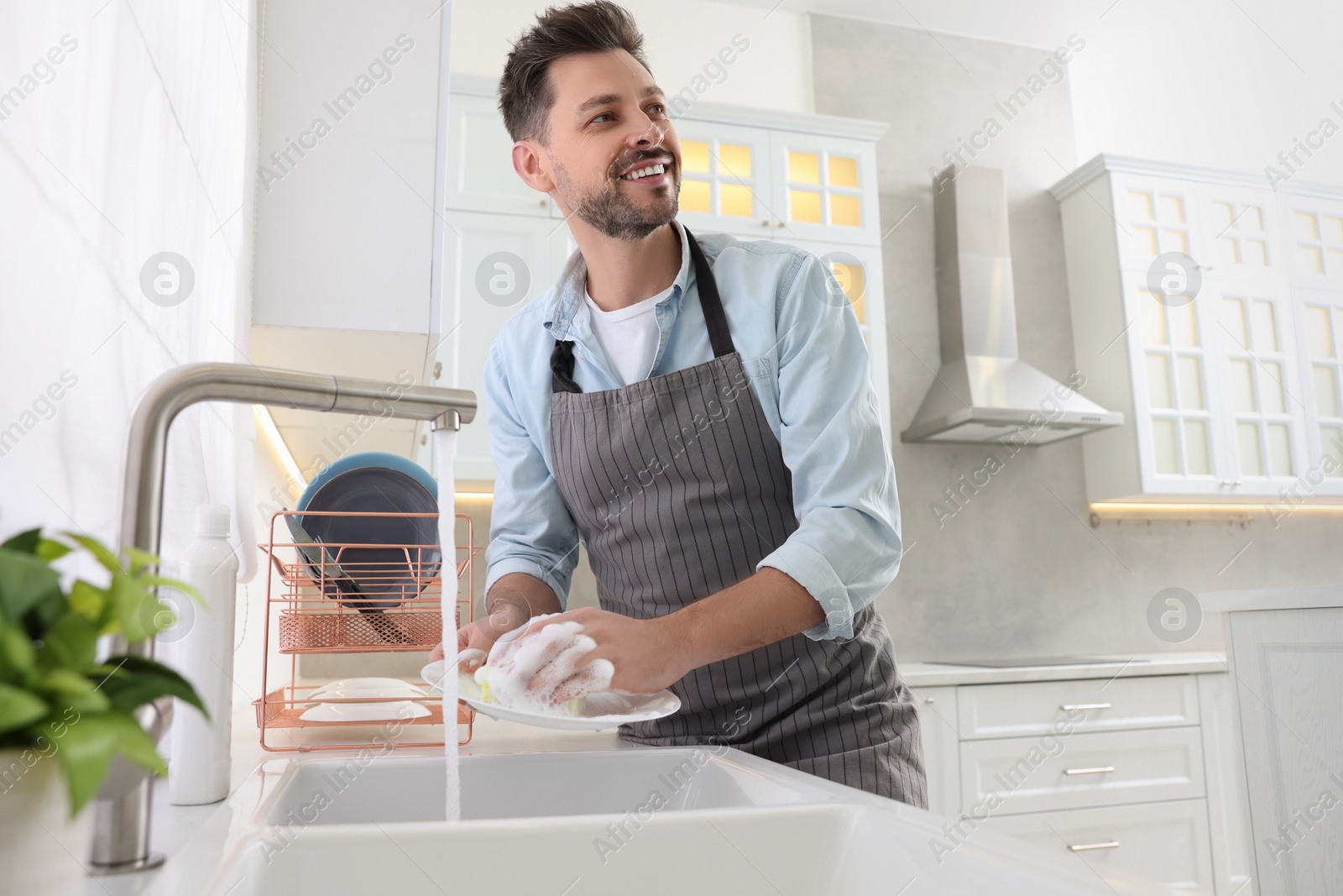 Photo of Man washing plate above sink in kitchen