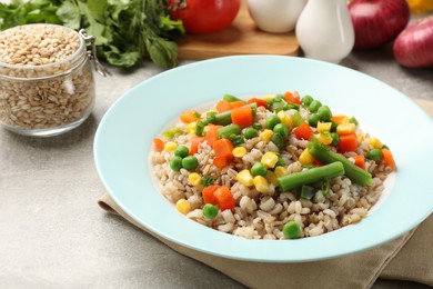 Photo of Tasty pearl barley porridge with vegetables on light textured table, closeup