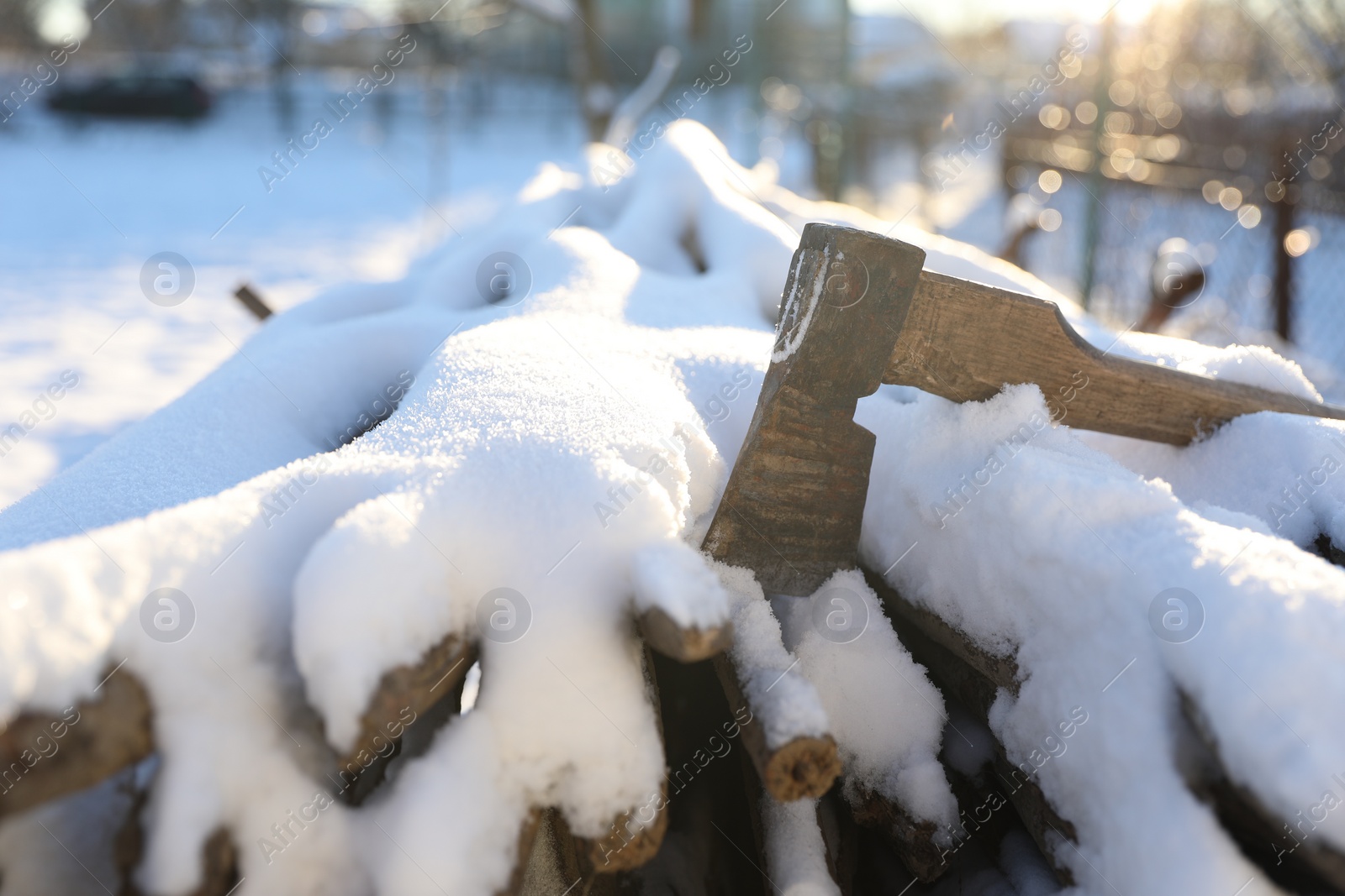 Photo of Metal axe on snowy firewood outdoors on sunny winter day