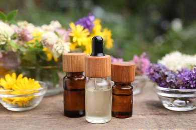 Bottles of essential oils and many beautiful flowers on wooden table