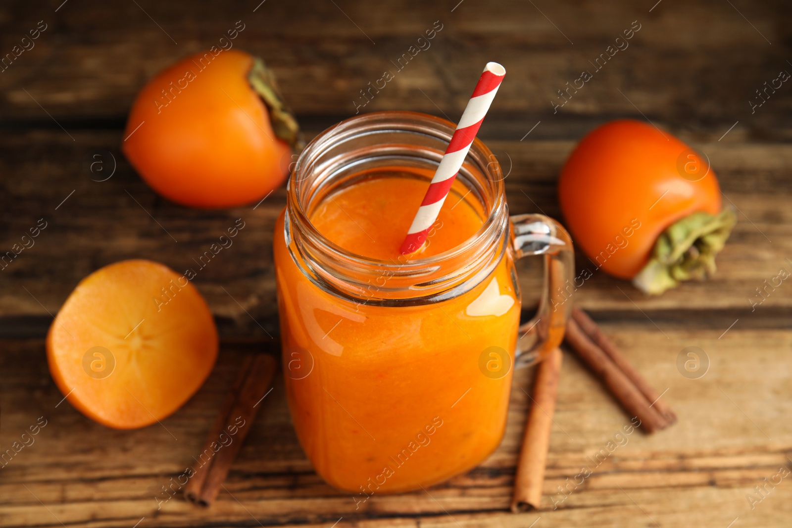 Photo of Tasty persimmon smoothie with straw on wooden table, closeup