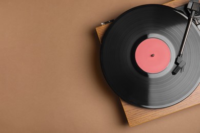 Photo of Modern vinyl record player with disc on brown background, top view. Space for text