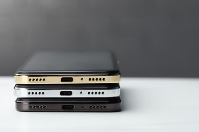 Photo of Stack of modern smartphones on white table, closeup. Space for text