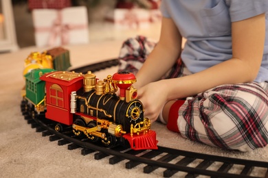 Photo of Little boy playing with colorful train toy in room decorated for Christmas, closeup