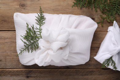 Furoshiki technique. Gifts packed in white fabric and thuja branches on wooden table, flat lay
