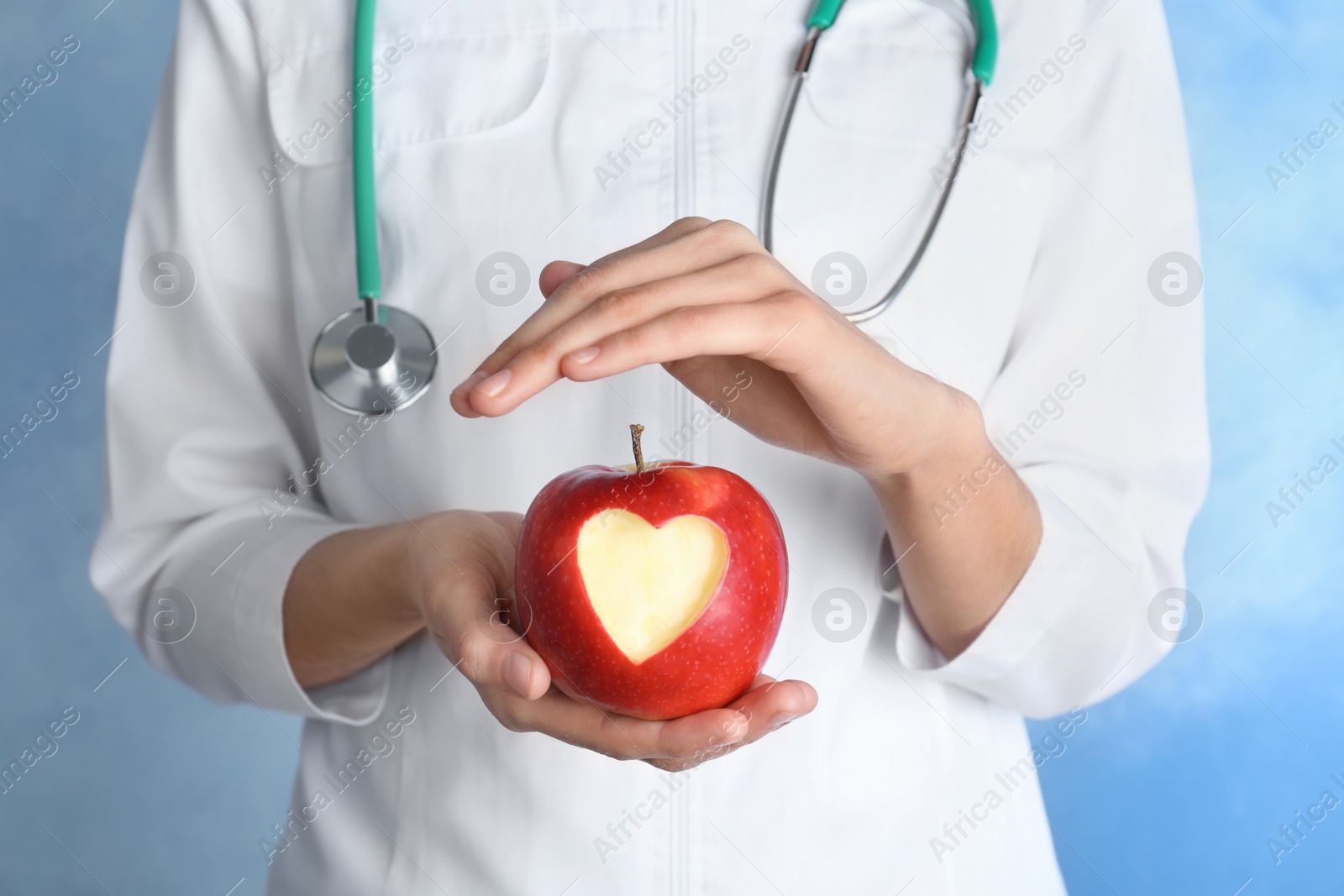 Photo of Woman holding apple with carved heart on color background, closeup
