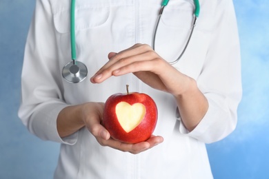 Woman holding apple with carved heart on color background, closeup