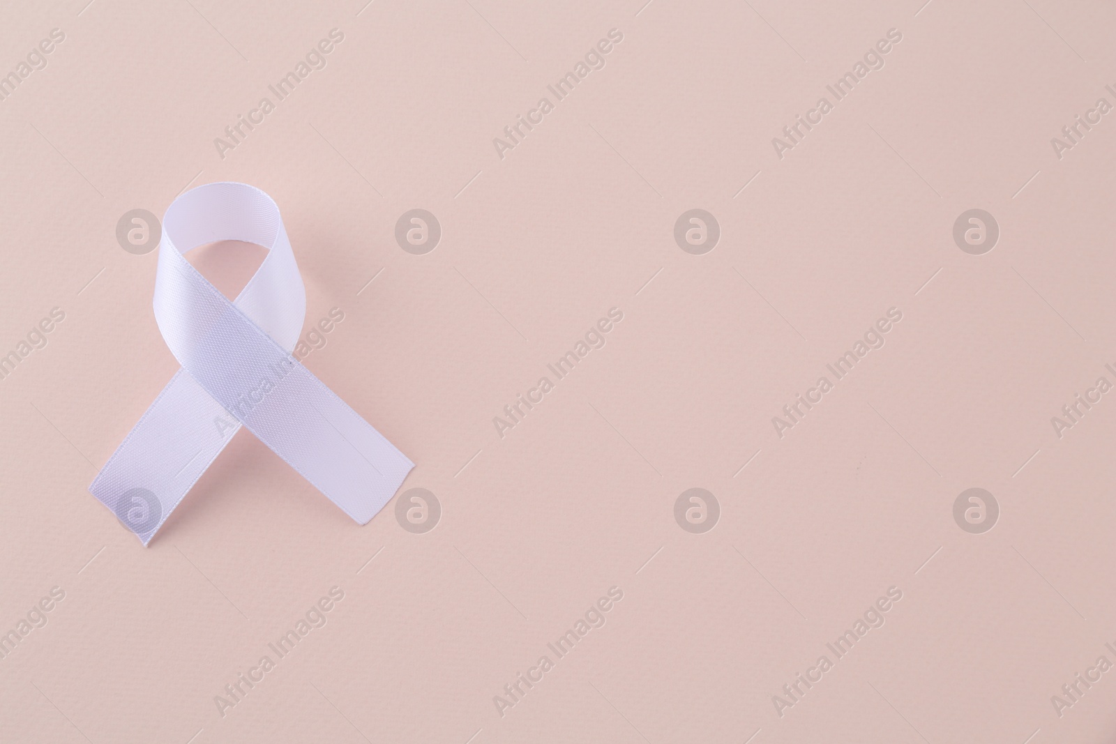 Photo of White awareness ribbon on beige background, top view. Space for text