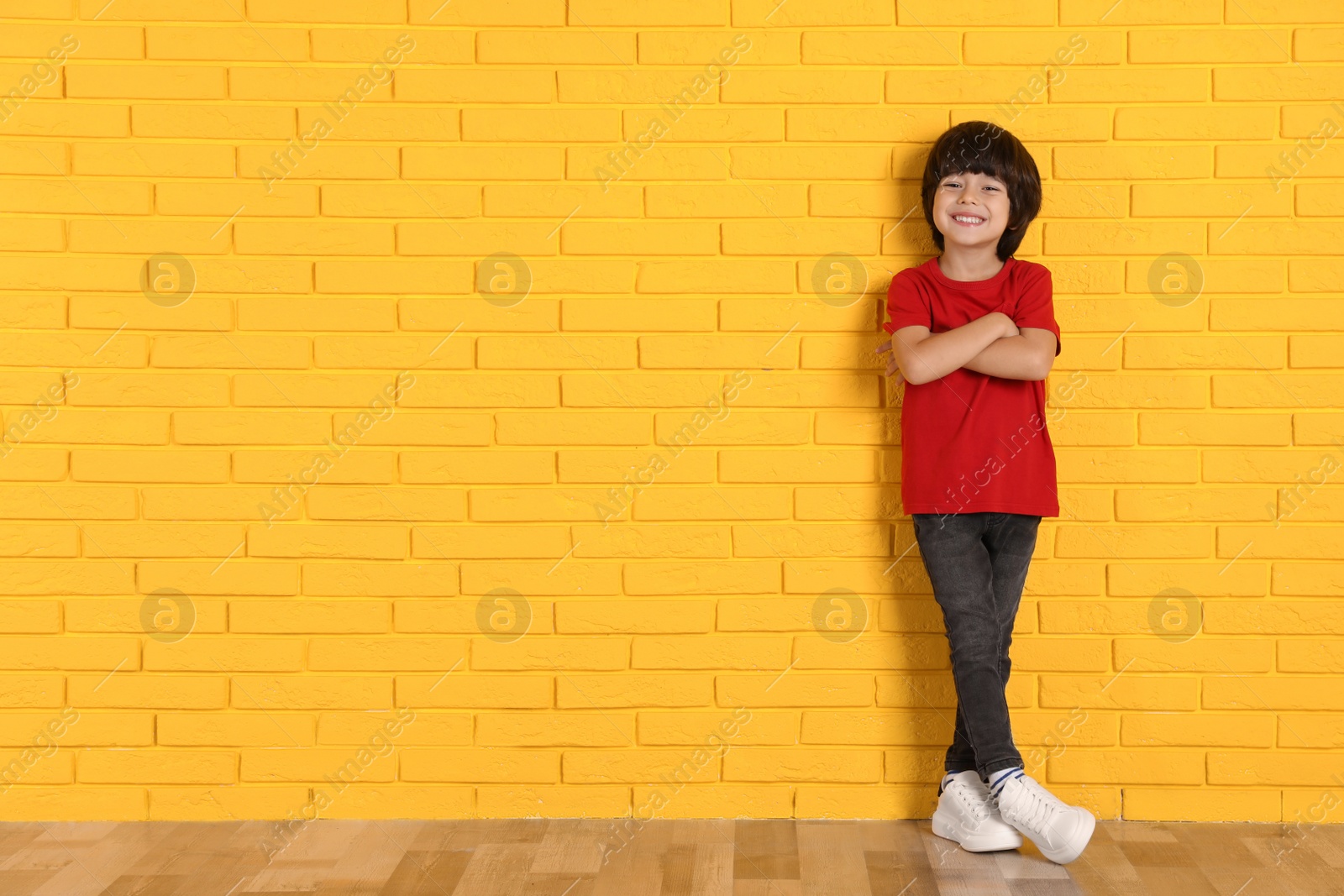 Photo of Cute little boy near yellow brick wall indoors, space for text