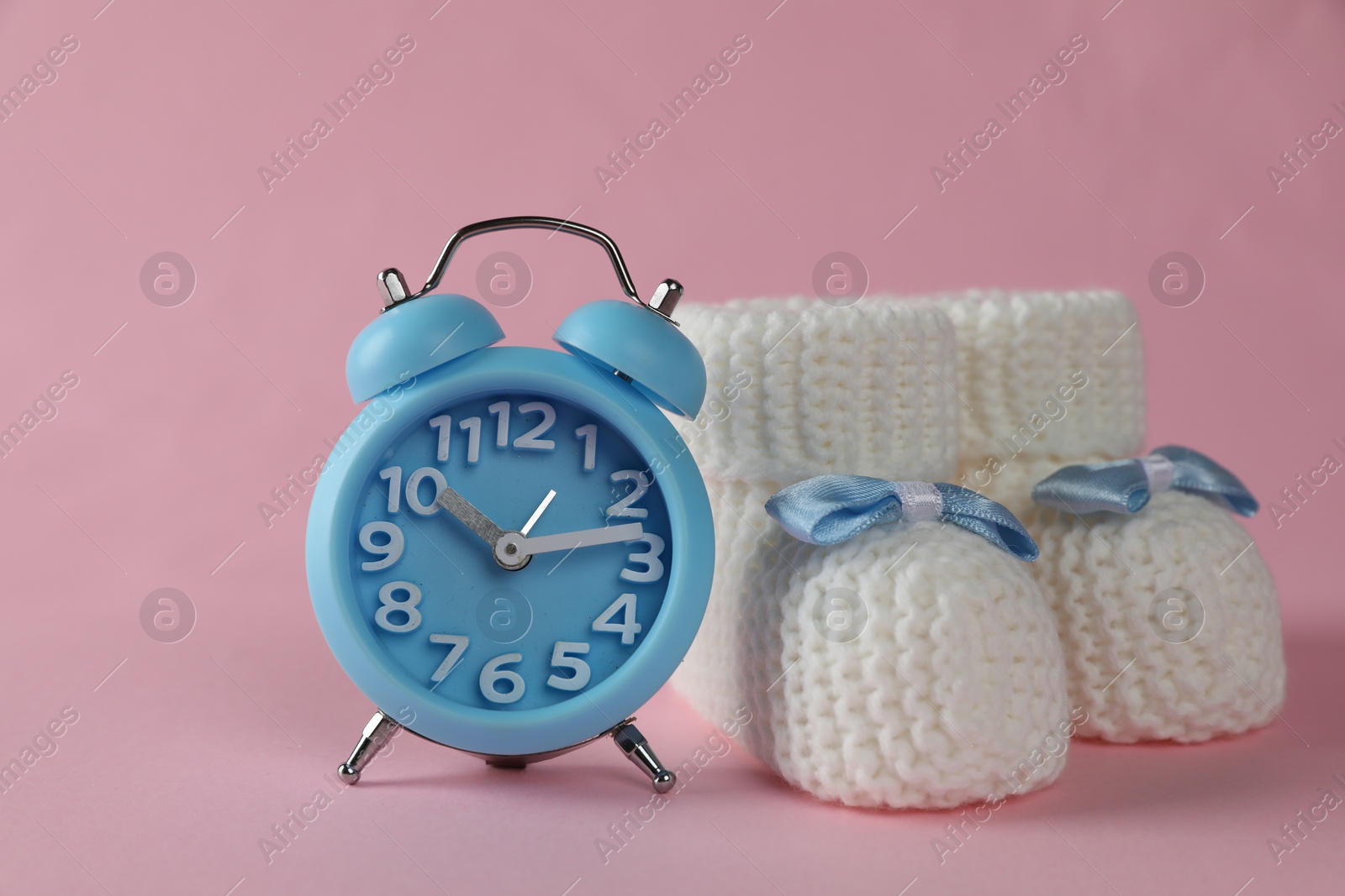 Photo of Alarm clock and baby booties on pink background. Time to give birth
