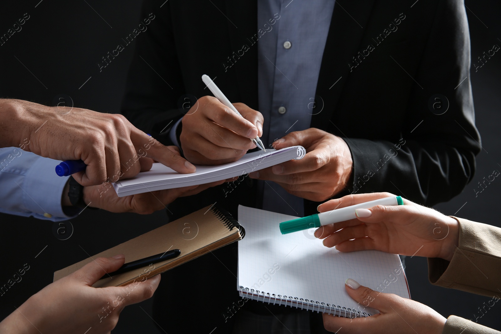 Photo of Man signing autograph in notebooks on dark background, closeup