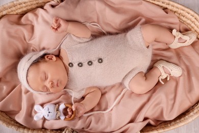 Cute newborn baby sleeping with rattle in wicker crib indoors, top view