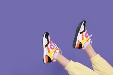 Woman wearing pair of new stylish sneakers on purple background, closeup