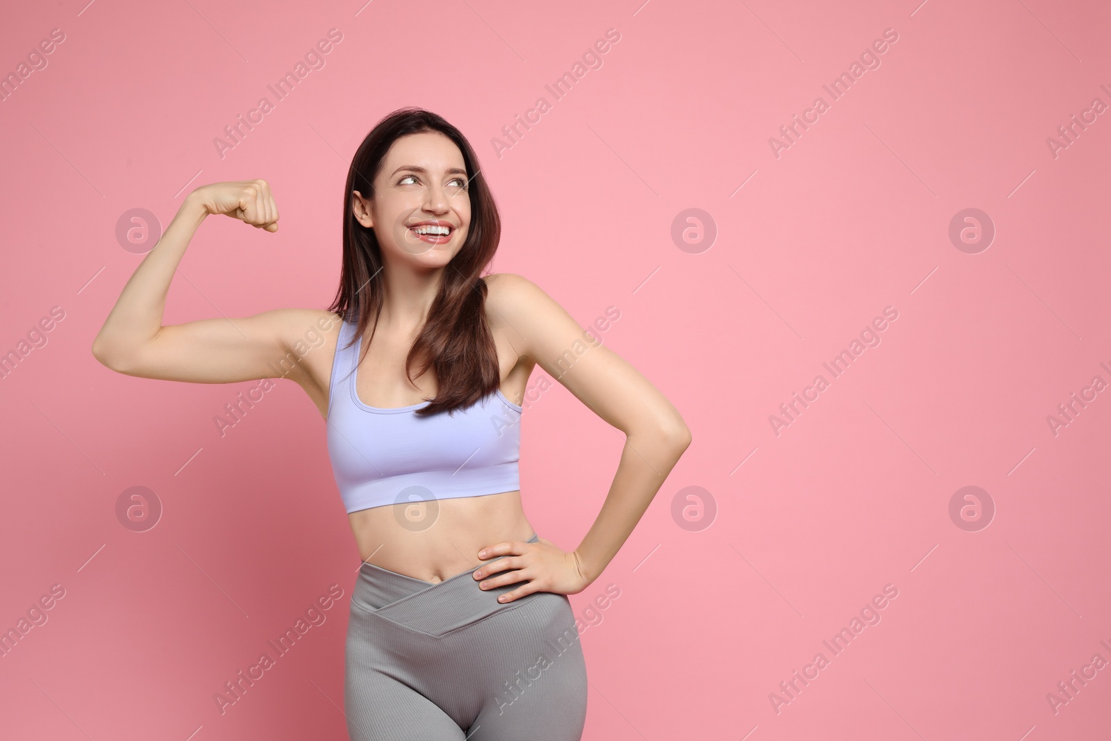 Photo of Happy young woman with slim body showing her muscles on pink background, space for text