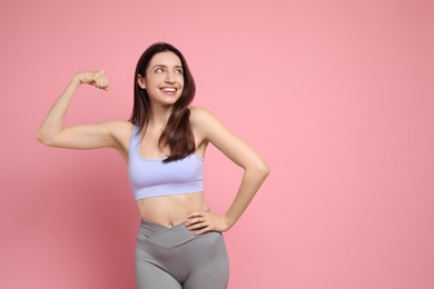 Photo of Happy young woman with slim body showing her muscles on pink background, space for text