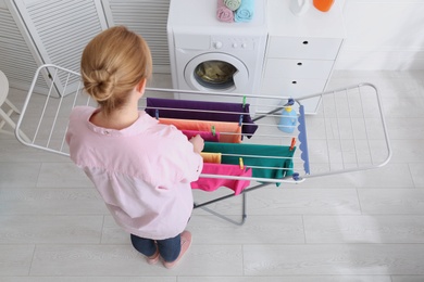 Photo of Woman hanging clean laundry on drying rack indoors, above view