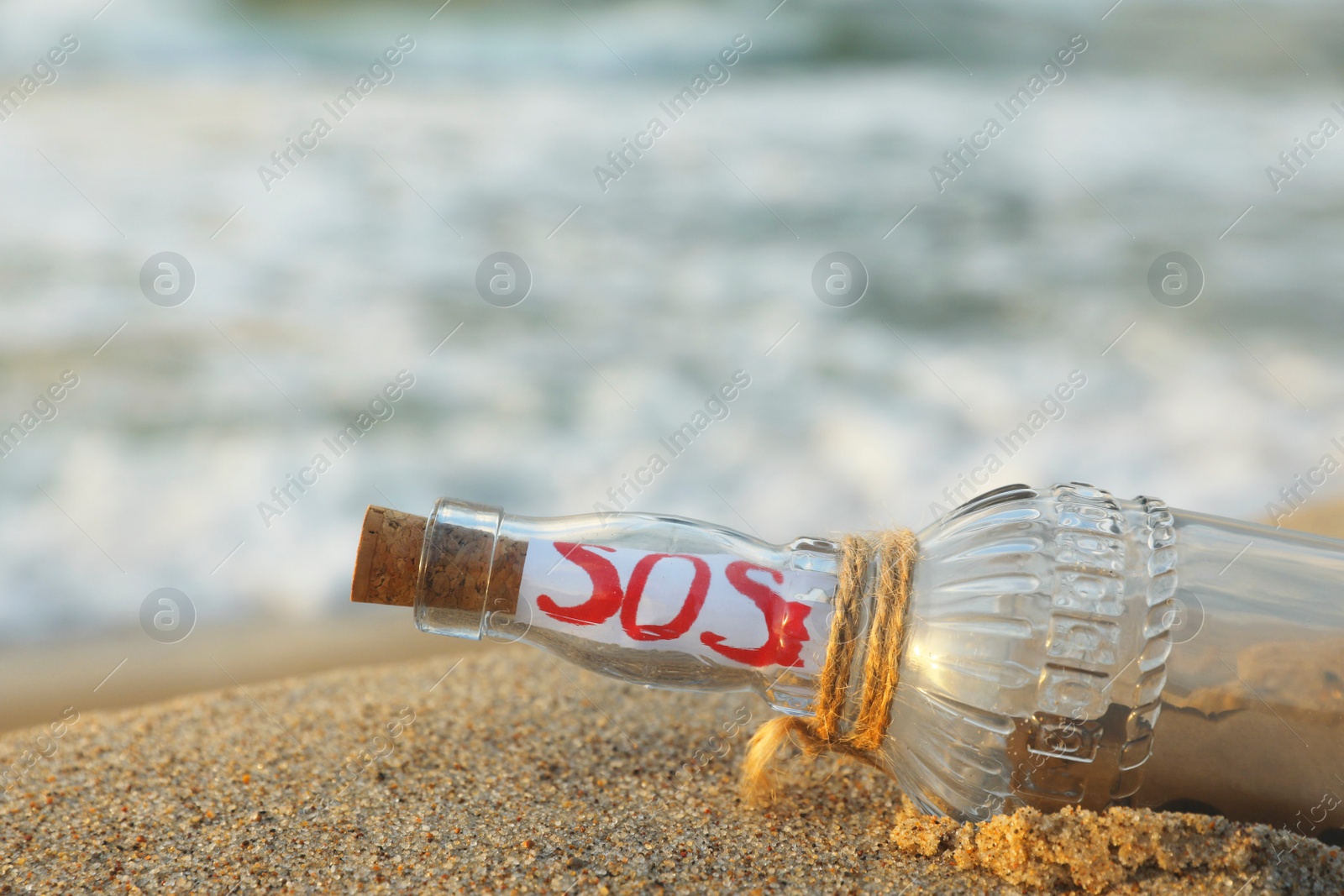 Photo of Glass bottle with SOS message on sand near sea, closeup