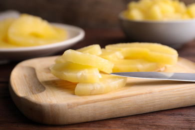 Photo of Canned pineapple pieces and knife on wooden board, closeup