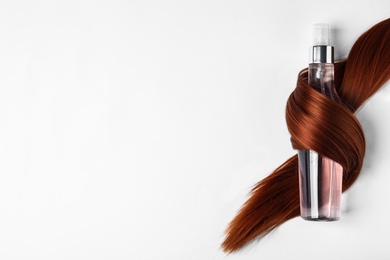 Spray bottle wrapped in lock of hair on white background, top view. Natural cosmetic products