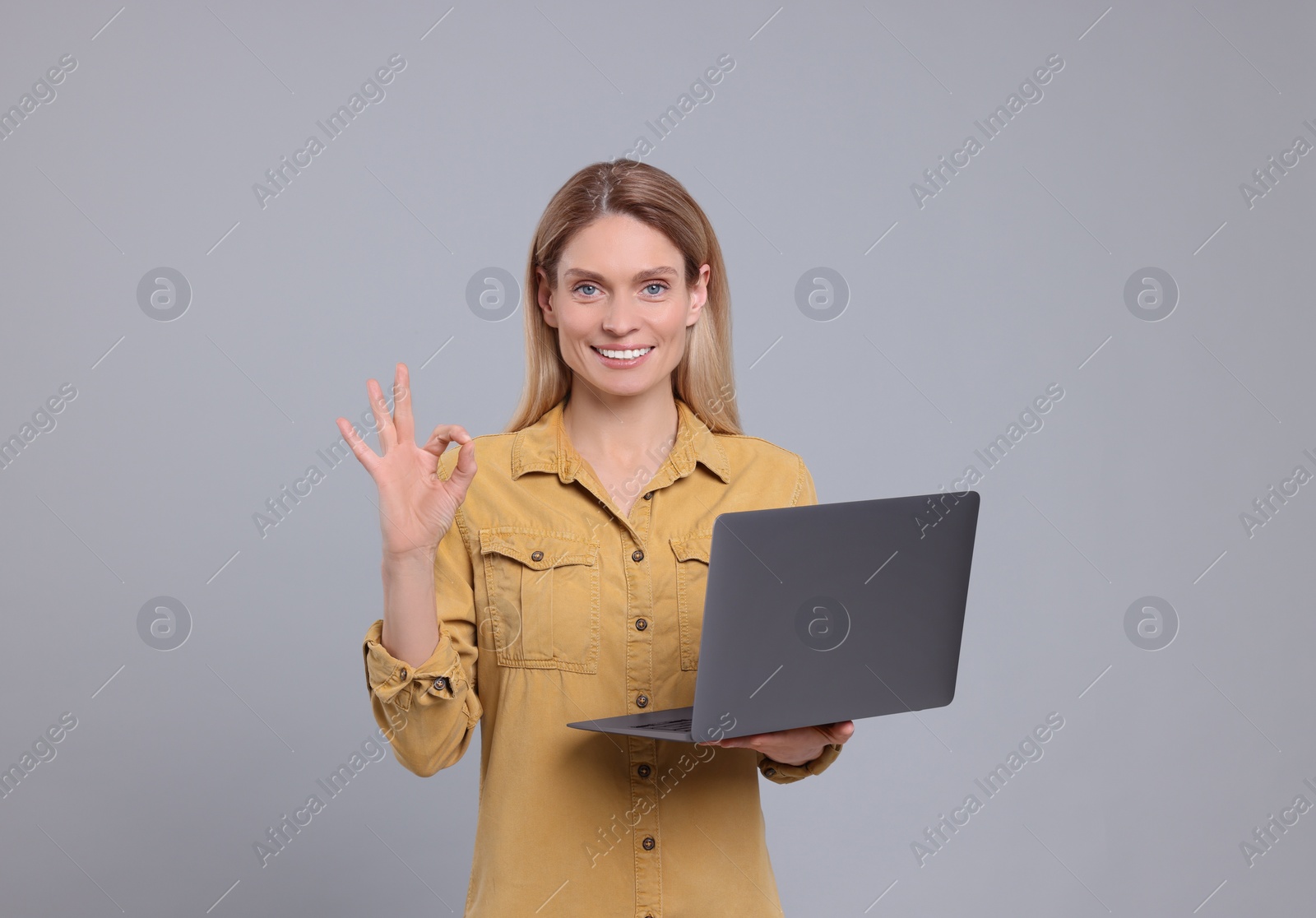 Photo of Happy woman with laptop showing ok gesture on light grey background