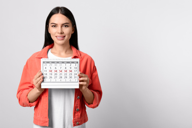 Photo of Young woman holding calendar with marked menstrual cycle days on light background. Space for text