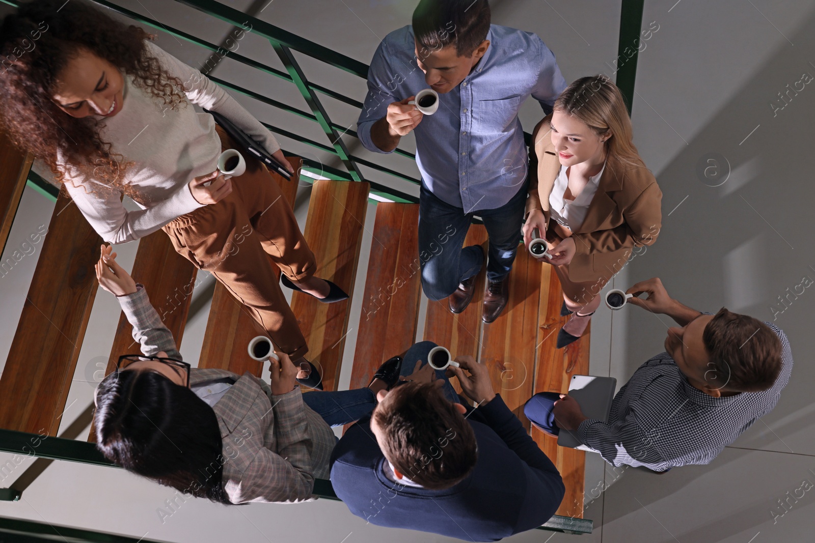 Photo of Group of coworkers talking during coffee break on stairs in office, top view