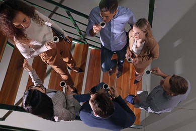 Group of coworkers talking during coffee break on stairs in office, top view