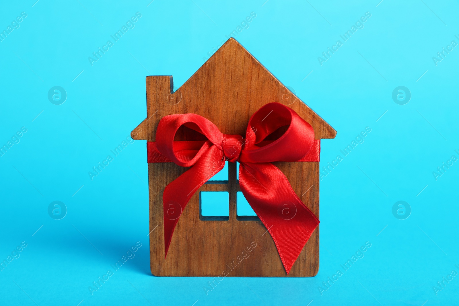 Photo of Wooden house model with red bow on light blue background. Housewarming party