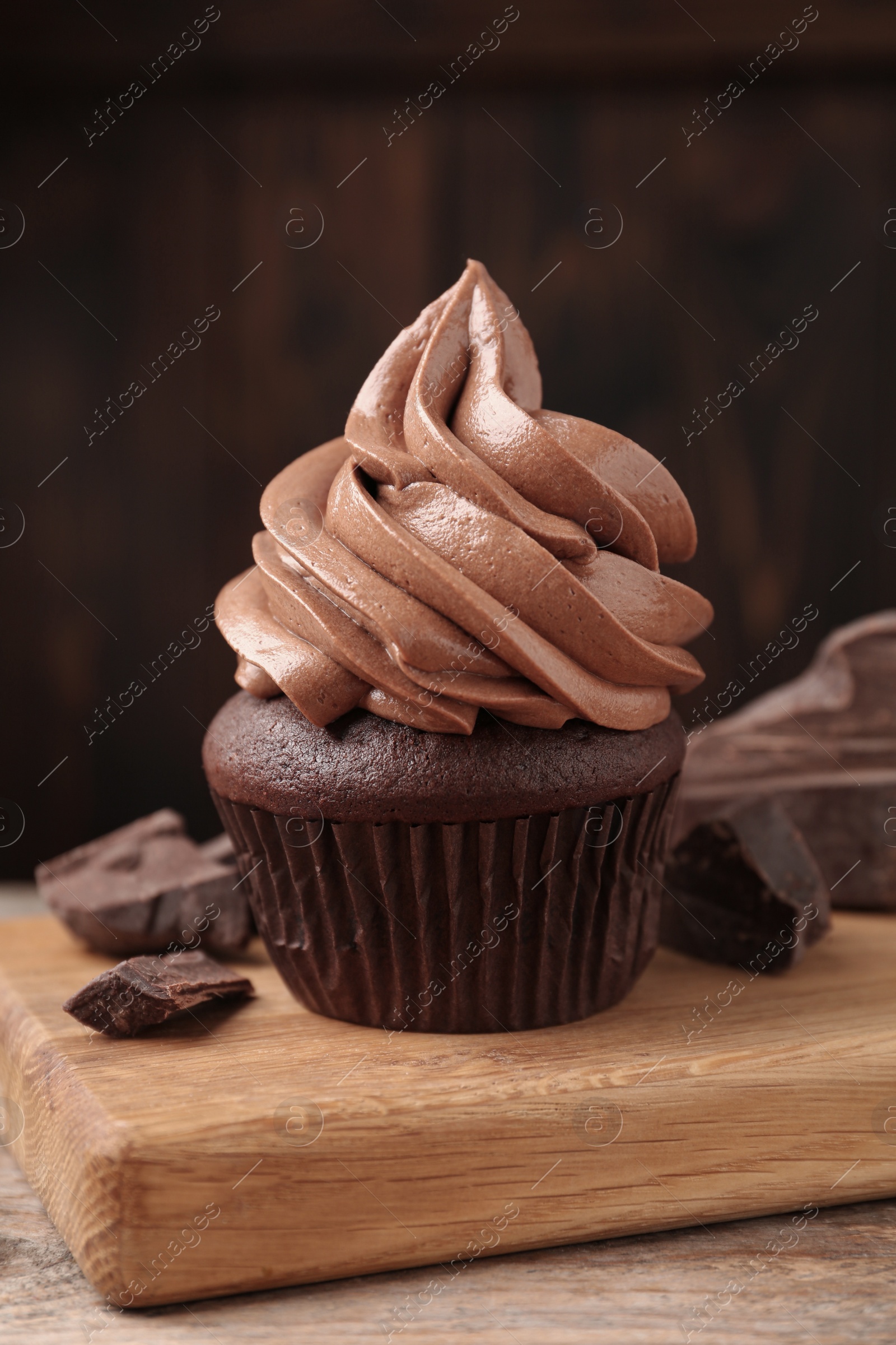 Photo of Delicious cupcake with cream and chocolate pieces on wooden table, closeup