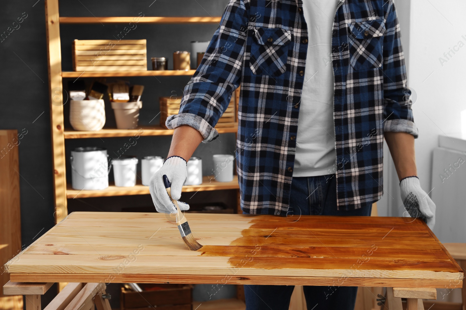 Photo of Man with brush applying wood stain onto wooden surface indoors, closeup