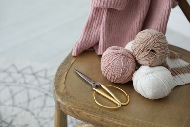 Yarn balls and scissors on wooden chair indoors, space for text. Creative hobby