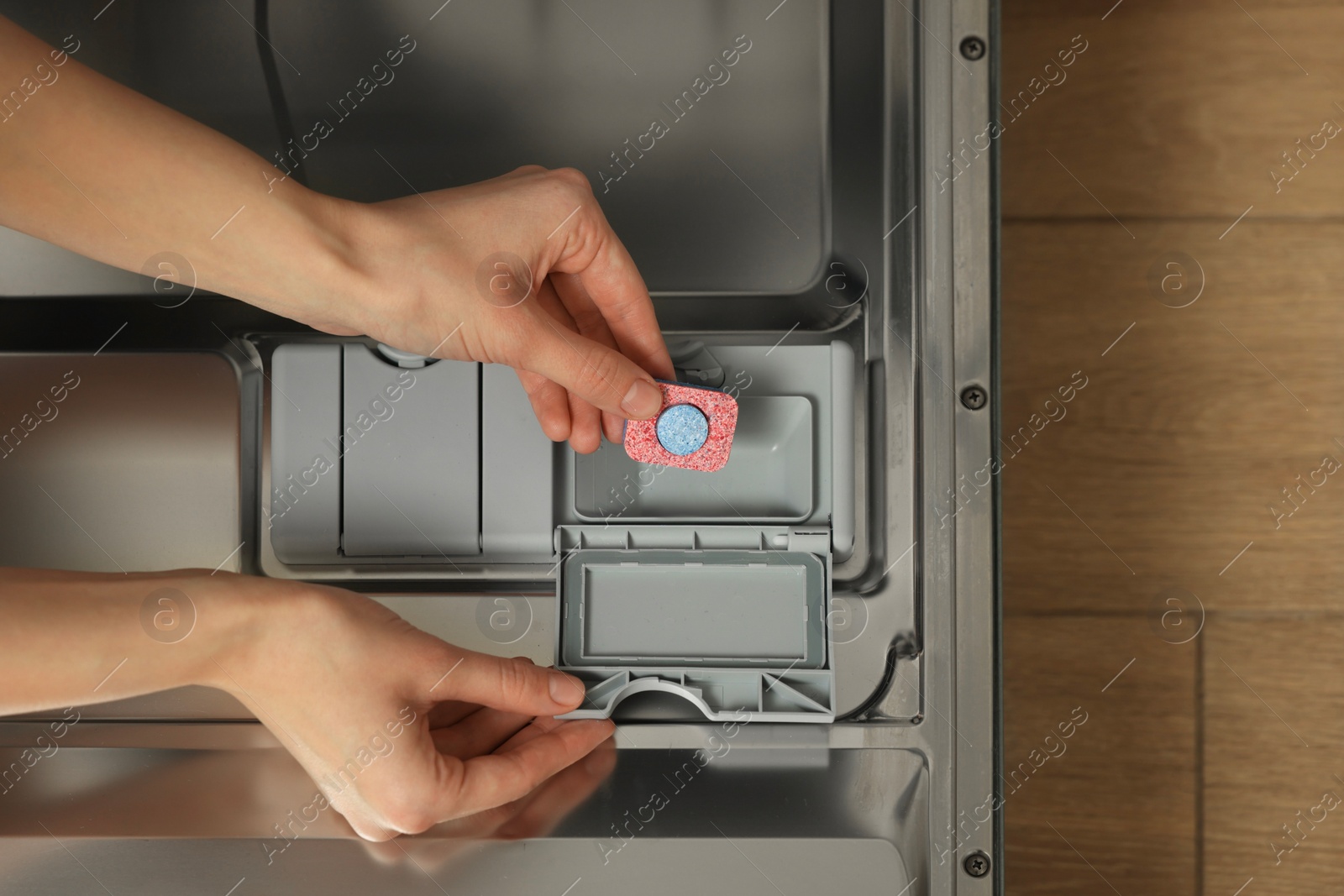 Photo of Woman putting detergent tablet into open dishwasher, top view